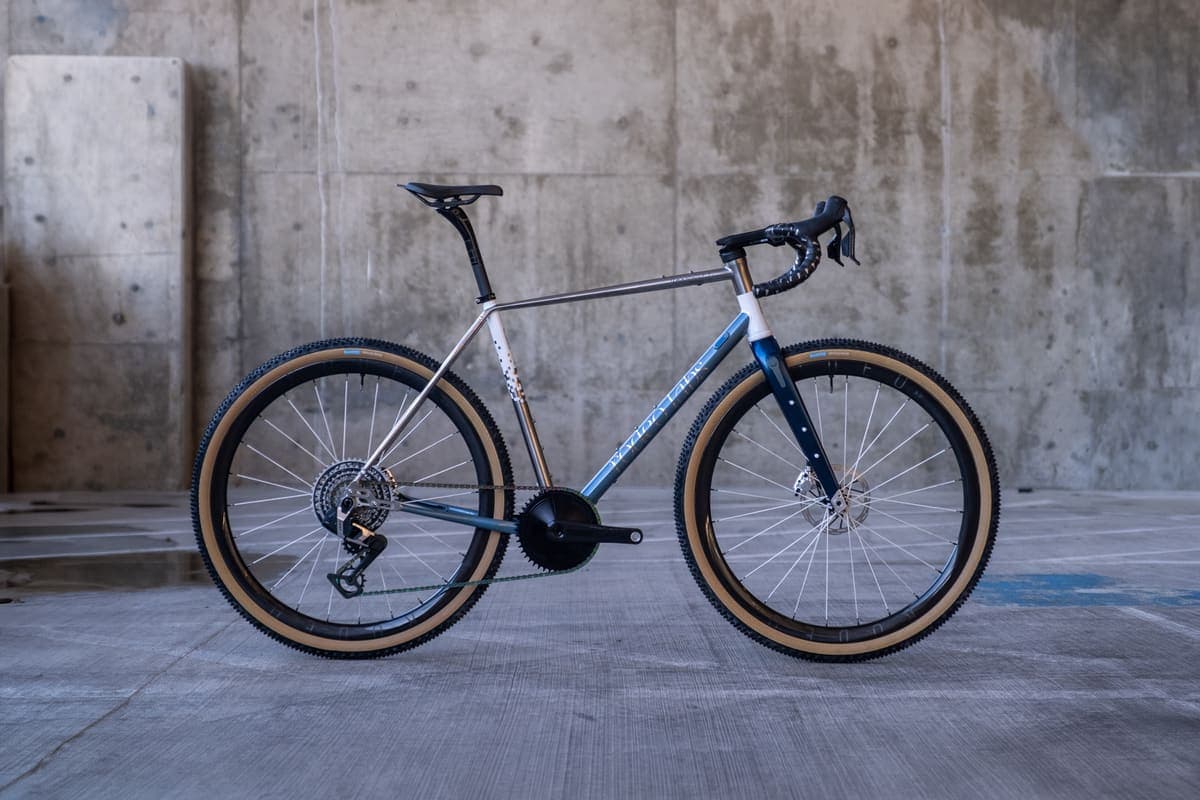 Komplett aufgebautes Rodeo-Labs-Bike von der Seite vor einer Betonwand — Stahlrahmen, blaue Gabel, beige Reifenflanken
